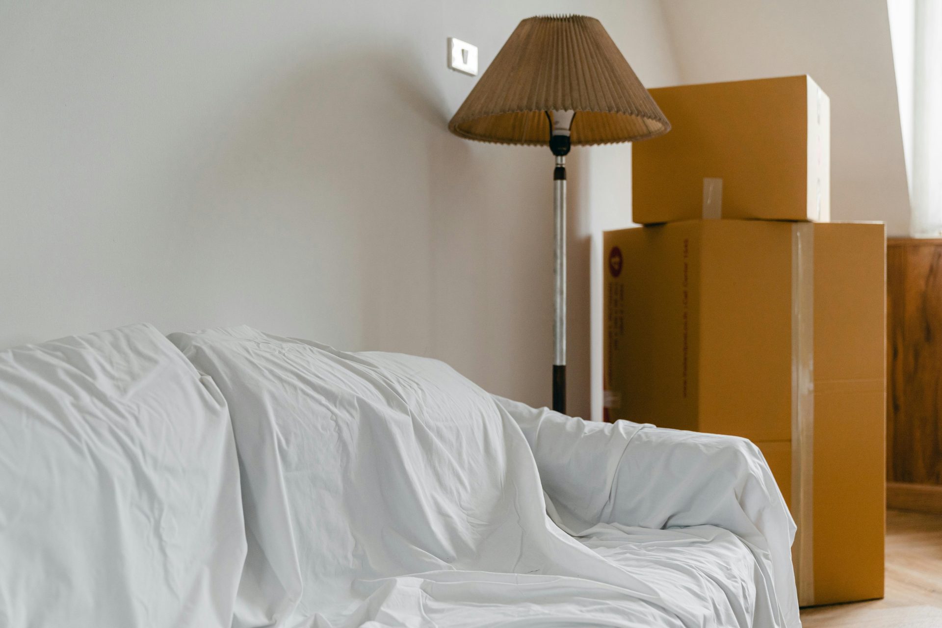 In einem hellen, geräumigen Zimmer eines neuen, modernen Hauses waren Sofa und Stehlampe mit Laken bedeckt und mit Kartons gefüllt.