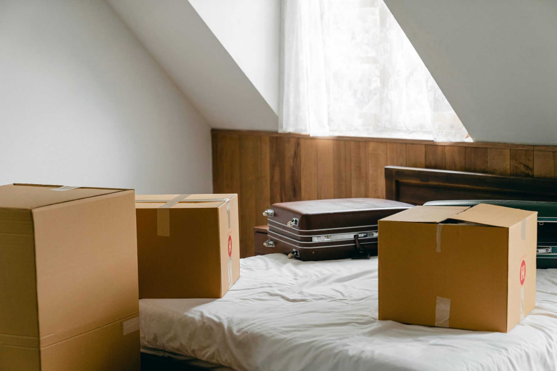 Kleine Pappkartons und Lederetuis lagen auf einem Bettlaken neben einem großen Karton in einem hellen Zimmer unter einem schrägen Dach.